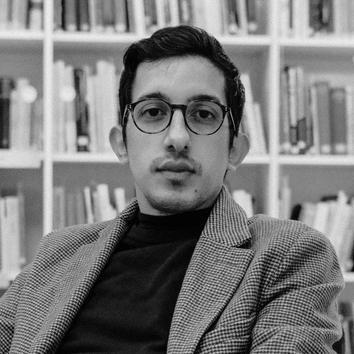 Portrait de Romain Mendez en noir et blanc, devant une bibliothèque.
